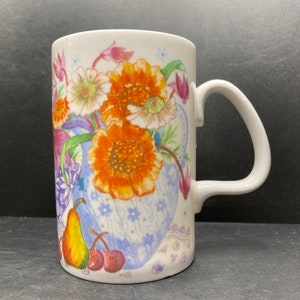May include: White ceramic mug with a floral design featuring orange, yellow, white, and pink flowers. The flowers are in a blue and white vase with a floral pattern. The mug has a white handle.