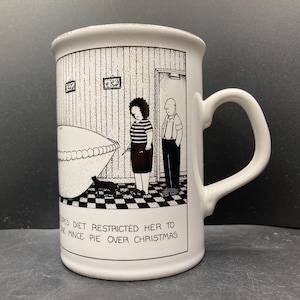 Peut inclure: Mug en céramique blanche avec une illustration de dessin animé en noir et blanc. L'illustration représente une femme, un homme et une tarte. Le texte sur la tasse se lit : "...le régime lui interdisait la tarte à la viande à Noël."