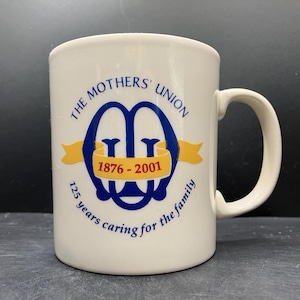 Może przedstawiać: Kremowy ceramiczny kubek z zakrzywionym uchwytem. Kubek zawiera niebieski napis "THE MOTHERS' UNION", a także niebieski i żółty emblemat oraz napis "1876-2001". Kubek ma również napis "125 years caring for the family".