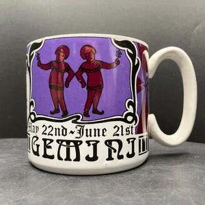 Op de afbeelding: Witte keramische mok met een Gemini-sterrenbeeldontwerp. De mok heeft een paarse achtergrond met twee figuren die takjes vasthouden. De tekst "May 22nd~June 21st" en "GEMINI" is op de mok gedrukt.
