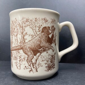 May include: A white ceramic mug with a brown illustration of a monkey in a tree. The monkey is holding a leaf in its mouth.