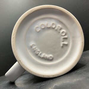 Puede incluir: Una taza de cer&aacute;mica blanca con asa, vista desde abajo. La base presenta el texto en relieve "COLOROLL ENGLAND" en un c&iacute;rculo. La taza tiene un dise&ntilde;o sencillo y cl&aacute;sico.