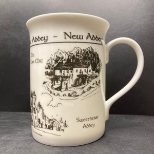 May include: White ceramic mug with a black and white illustration of a building and the text "Sweetheart Abbey" and "New Abbey".