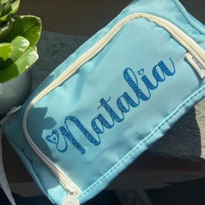 May include: A light blue zippered pouch with a white zipper and a white label that says "oddblue". The pouch has the name "Natalia" written in blue glitter letters with a small heart in front of the name.