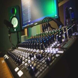 May include: A black audio mixing board with multiple knobs and sliders. The board has a variety of colored buttons and is connected to a computer monitor.
