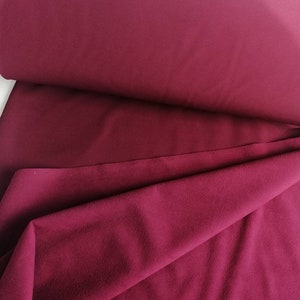 May include: A close-up of a deep burgundy fabric. The fabric is folded and has a soft, textured surface.