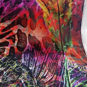 Op de afbeelding: Abstracte stof met een kleurrijk ontwerp met een grote veer, dierenprint en een draaiend patroon in tinten rood, roze, geel, groen en blauw.