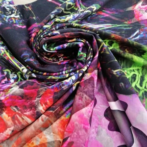 Op de afbeelding: Close-up van een kleurrijke stof met een draaiende print. De stof is gemaakt van een zacht, zijdeachtig materiaal en heeft een verscheidenheid aan kleuren, waaronder roze, paars, groen en blauw.