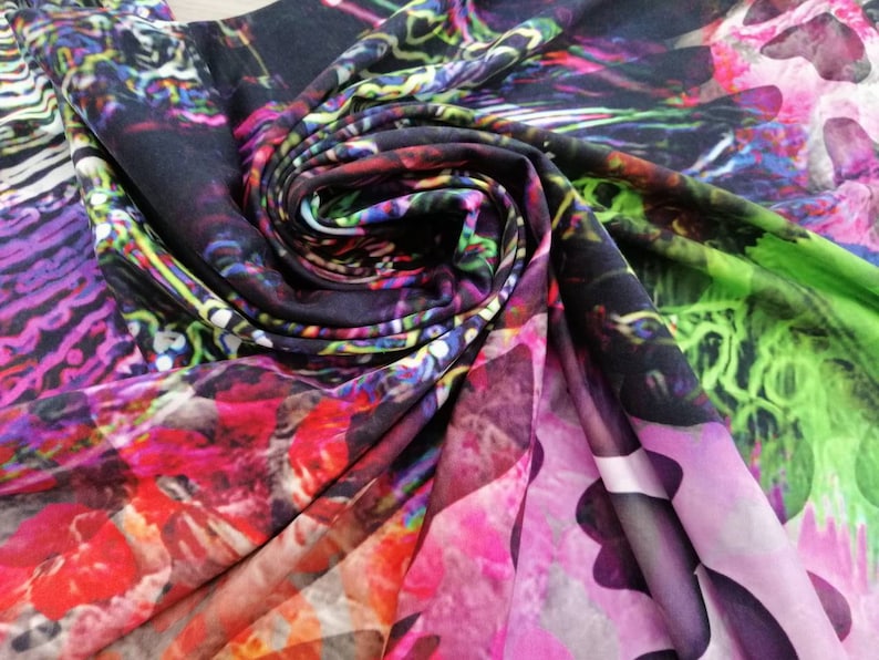 Op de afbeelding: Close-up van een kleurrijke stof met een draaiende print. De stof is gemaakt van een zacht, zijdeachtig materiaal en heeft een verscheidenheid aan kleuren, waaronder roze, paars, groen en blauw.