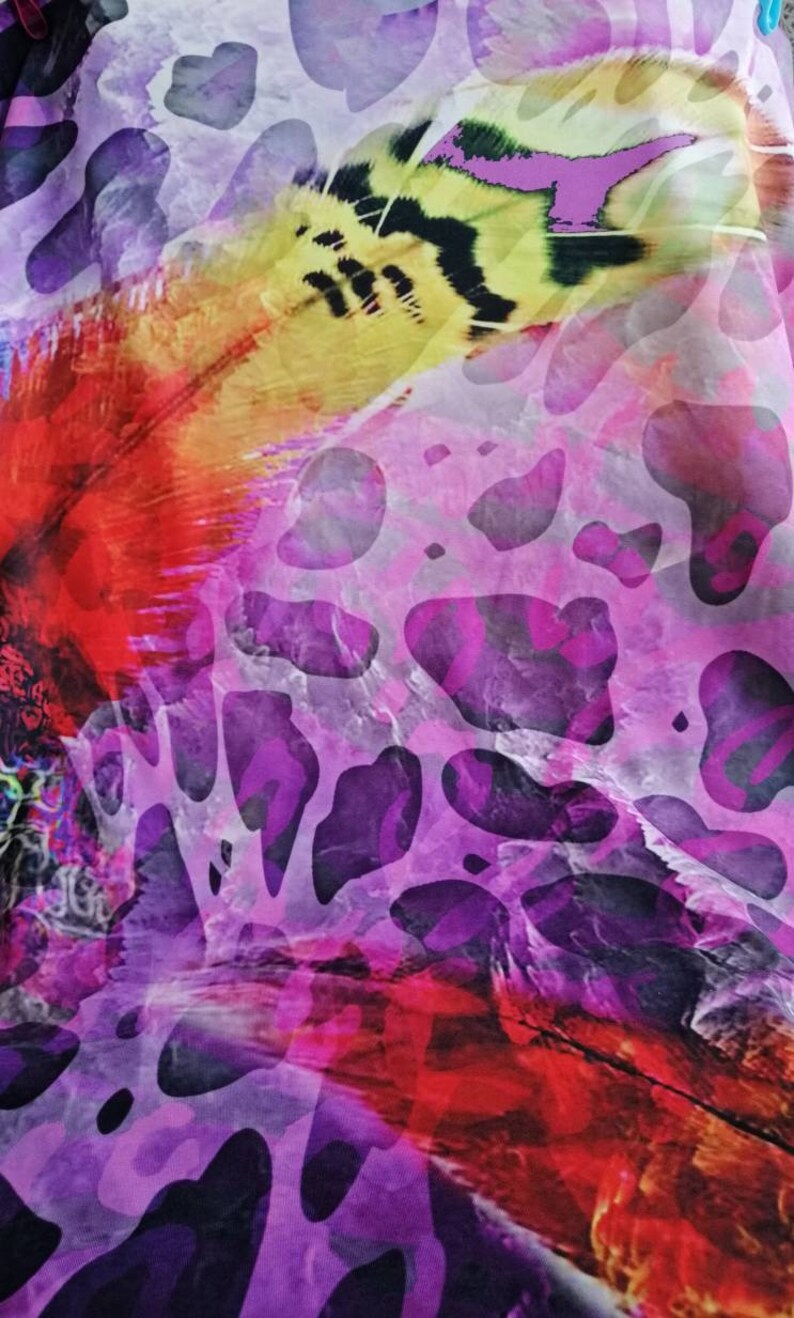 Op de afbeelding: Abstracte stof met een paars, roze en geel patroon. De stof heeft een groot, kleurrijk verenontwerp met zwarte en witte markeringen.