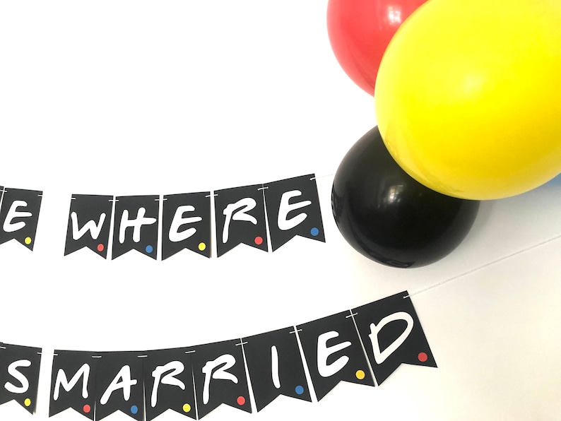 May include: Black and white banner with the text "We Were Married" in a white font. The banner is decorated with colorful dots. The banner is hanging from a string. There are balloons in the background.