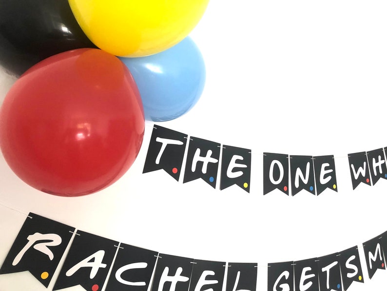 May include: Black and white banner with the text "The One Where Rachel Gets Married" in a white handwritten font. The banner is decorated with colorful dots. The banner is hanging from balloons in red, yellow, and blue.