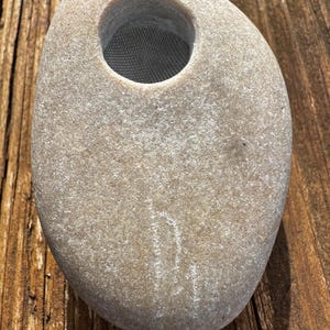 May include: A smooth, grey stone with a round opening and a mesh screen inside. The stone is carved to look like a vase.