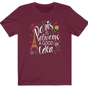 May include: A maroon t-shirt with a white graphic design that says "Paris is always a good idea" with a drawing of the Eiffel Tower and floral accents.
