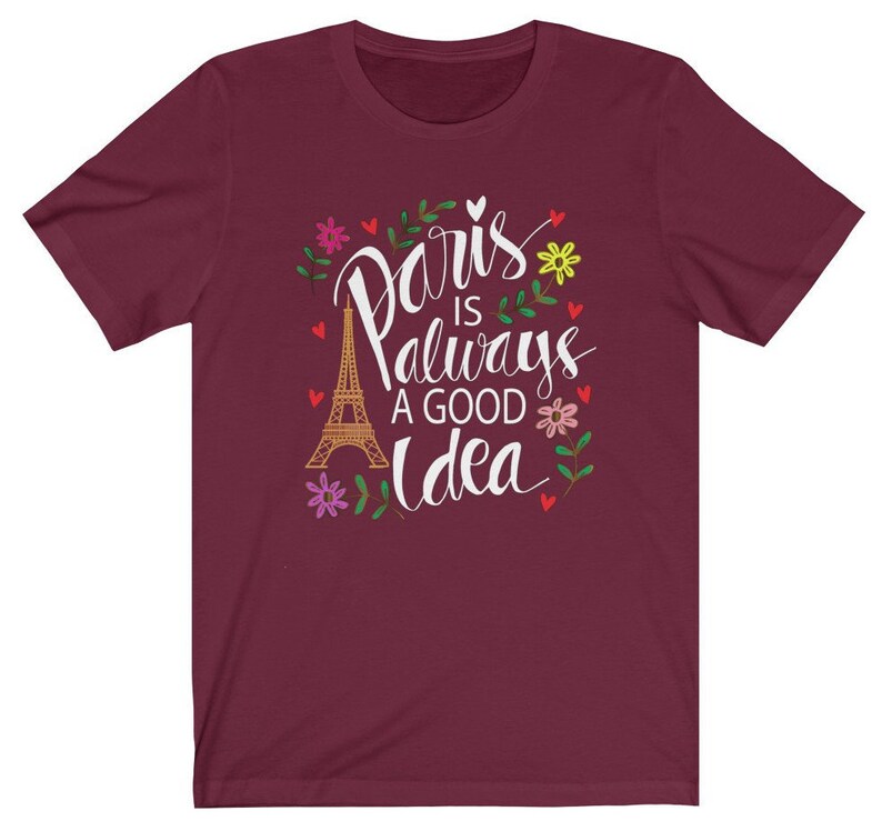 May include: A maroon t-shirt with a white graphic design that says "Paris is always a good idea" with a drawing of the Eiffel Tower and floral accents.