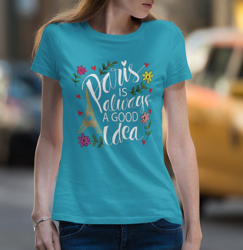 May include: A turquoise blue t-shirt with a white graphic print of the Eiffel Tower and the text "Paris is always a good idea" surrounded by flowers and hearts.