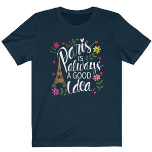 May include: A navy blue t-shirt with a white graphic design featuring the Eiffel Tower and the text "Paris is always a good idea" surrounded by flowers.