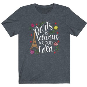 May include: A dark heather grey t-shirt with a white graphic design featuring the Eiffel Tower and the text "Paris is always a good idea". The graphic is surrounded by colorful flowers and hearts.