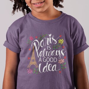 May include: Purple t-shirt with a white graphic that says "Paris is always a good idea" with a drawing of the Eiffel Tower and flowers.