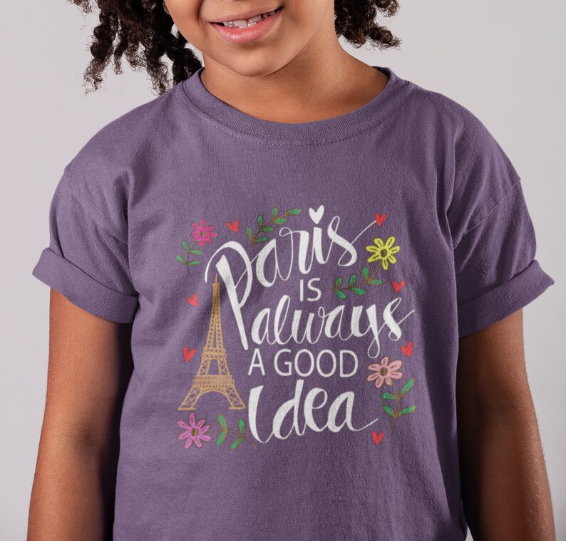 May include: Purple t-shirt with a white graphic that says "Paris is always a good idea" with a drawing of the Eiffel Tower and flowers.