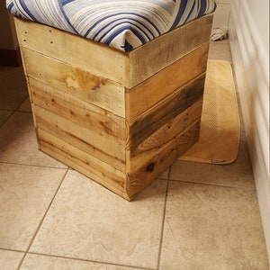 May include: A wooden storage ottoman with a blue and white patterned fabric top. The ottoman is made from reclaimed wood planks.