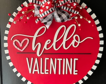 May include: Red and white round door hanger with a black and white checkered bow, red and white berries, and the text "hello valentine" in white lettering.