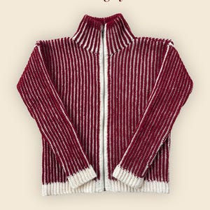 Puede incluir: Un suéter con cremallera a rayas burdeos y blancas con cuello alto. El suéter presenta una cremallera plateada de largo completo y puños y dobladillo de canalé blancos. La marca "mogily" se muestra en la parte superior.