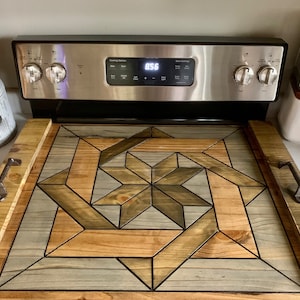 May include: A wooden stovetop tray with a geometric design in shades of brown, gray, and black. The tray has two metal handles on the sides.