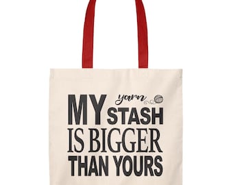 May include: A white canvas tote bag with red handles. The bag has black text that reads "yarn stash is bigger than yours".