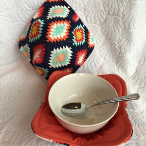 Puede incluir: Un tazón de cerámica blanco con una cuchara dentro, sentado en un posavasos estampado en rojo y azul. El posavasos está sobre una superficie blanca y esponjosa.