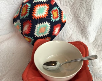 Peut inclure: Un bol en céramique blanche avec une cuillère à l'intérieur, posé sur un dessous de plat à motifs rouge et bleu. Le dessous de plat est sur une surface blanche et moelleuse.