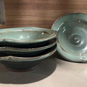 May include: Set of four teal ceramic bowls with a brown rim. The bowls are stacked on top of each other. The bowl on top has a swirl design.