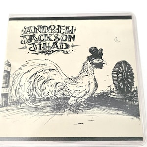 Könnte beinhalten: Schwarz-Weiß-Illustration auf cremefarbenem Hintergrund. Das Bild zeigt einen Hahn mit Hut, ein Riesenrad und den Text "ANDREW JACKSON JIHAD" in einer stilisierten Schriftart. Das Kunstwerk ist in einer transparenten Kunststoffhülle eingeschlossen.