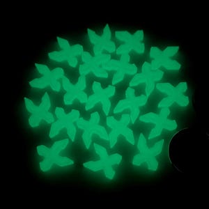 May include: A collection of glowing green, four-pointed star-shaped objects against a black background. The objects appear to be clustered together, emitting a soft, luminous glow. The overall effect is a vibrant, eye-catching display.