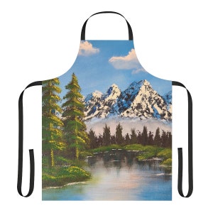 May include: A blue and white kitchen apron with a painting of a snowy mountain range and a lake in the foreground. The apron has black adjustable straps.