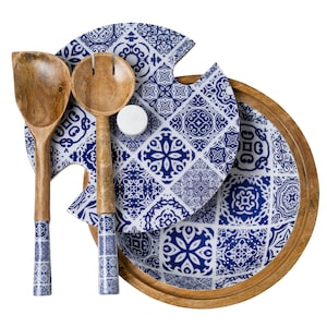 May include: A wooden serving tray with a round shape and a light brown finish. The tray holds a blue and white patterned plate and two wooden salad servers. The salad servers have blue and white patterned handles.