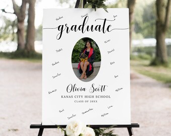 May include: White graduation sign with a photo of a graduate in a cap and gown. The sign says "graduate" in cursive and "Olivia Scott" in a decorative font. It also says "Kanas City High School" and "Class of 20XX".