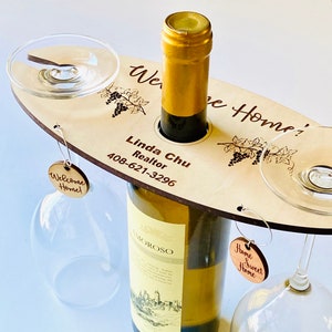 May include: Wooden wine bottle and glass holder with the text "Welcome Home!" and "Home Sweet Home" on tags. The holder also has the text "Linda Chu Realtor 408-621-3296" and a grapevine design.