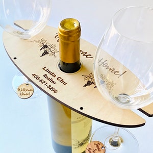 May include: Wooden wine bottle and glass holder with the text "Welcome Home!" and "Home Sweet Home" on two small wooden tags. The holder also has the text "Linda Chu Realtor 408-621-3296" engraved on it.