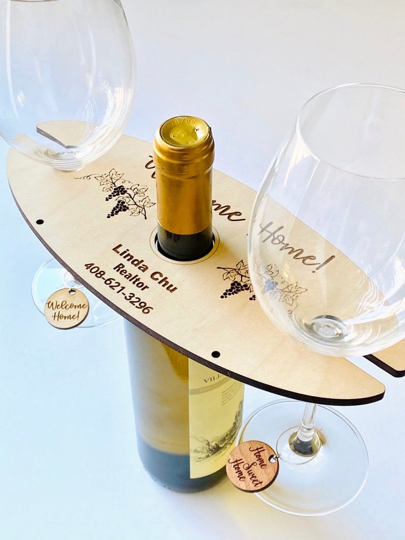 May include: Wooden wine bottle and glass holder with the text "Welcome Home!" and "Home Sweet Home" on two small wooden tags. The holder also has the text "Linda Chu Realtor 408-621-3296" engraved on it.