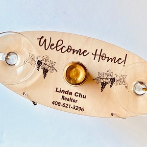 May include: Wooden serving tray with the text "Welcome Home!" and "Linda Chu Realtor 408-621-3296". The tray has two glass holders and a small round indentation for a bottle.