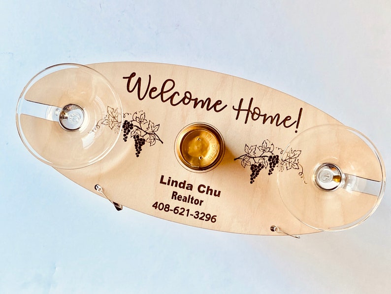 May include: Wooden serving tray with the text "Welcome Home!" and "Linda Chu Realtor 408-621-3296". The tray has two glass holders and a small round indentation for a bottle.