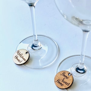 May include: Two wine glass charms with wooden round tags. One tag says "Welcome Home!" and the other says "Home Sweet Home".
