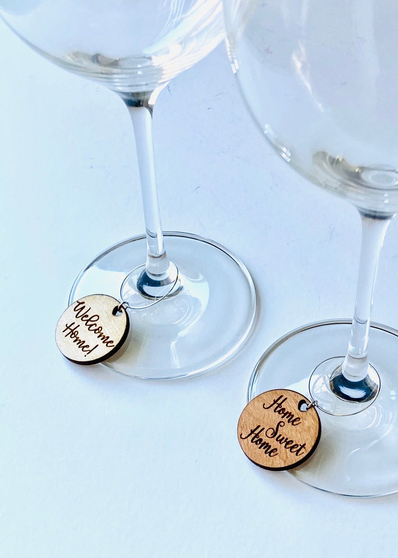 May include: Two wine glass charms with wooden round tags. One tag says "Welcome Home!" and the other says "Home Sweet Home".