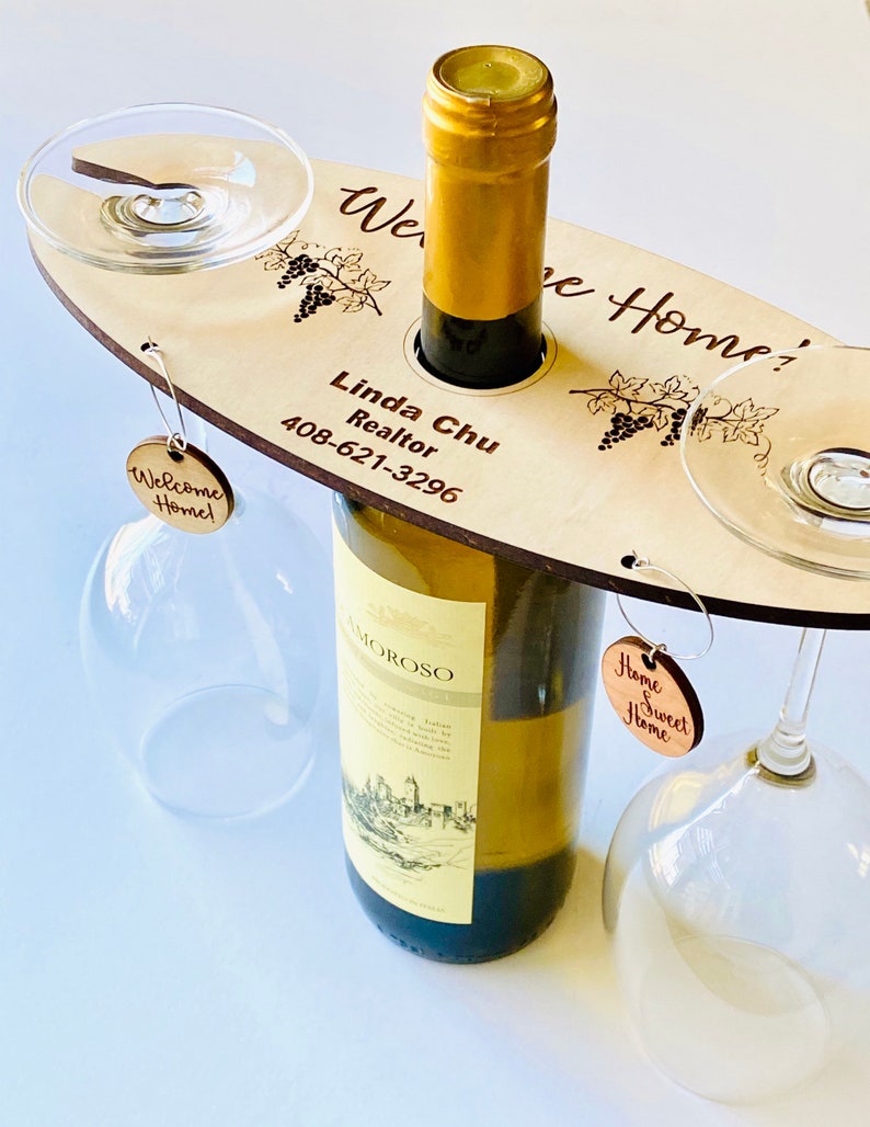 May include: Wooden wine bottle and glass holder with the text "Welcome Home!" and "Home Sweet Home" on tags. The holder also has the text "Linda Chu Realtor 408-621-3296" and a grapevine design.