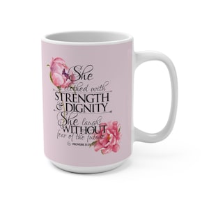 Könnte beinhalten: Weiße Keramik-Tasse mit hellrosa Hintergrund. Die Tasse zeigt den Text "She clothed with STRENGTH & DIGNITY She laughs WITHOUT fear of the future" mit floralen Akzenten. Die Tasse hat einen weißen Griff.