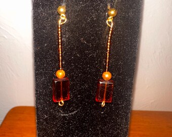 May include: A pair of long dangle earrings with gold beads and a rectangular amber-colored bead at the bottom.