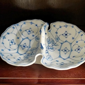 May include: A white ceramic serving dish with a blue and white floral pattern. The dish has two sections and a handle in the center.