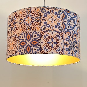 Könnte beinhalten: Ein weißer Lampenschirm mit einem blauen und orangefarbenen geometrischen Muster. Der Lampenschirm hat eine goldene Auskleidung.