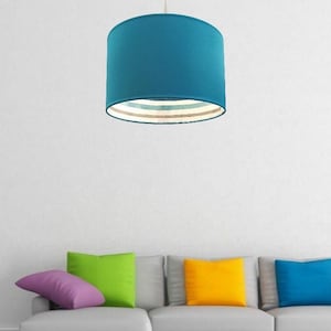 Può includere: Un paralume blu turchese con un bordo a righe bianco, beige e blu chiaro. Il paralume è appeso al soffitto sopra un divano grigio con cuscini colorati.